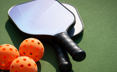 Three orange pickleballs and two paddles set on a court